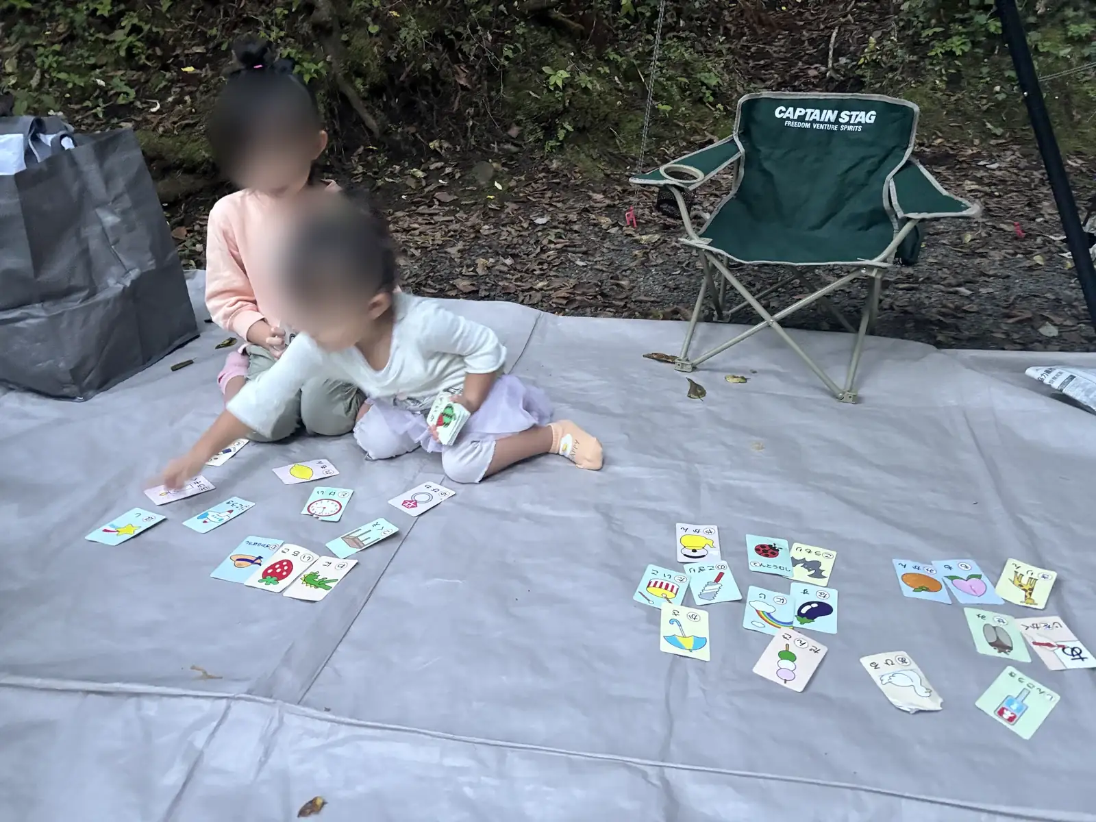 キャンプサイトのシート上でカード遊びをする子どもたち